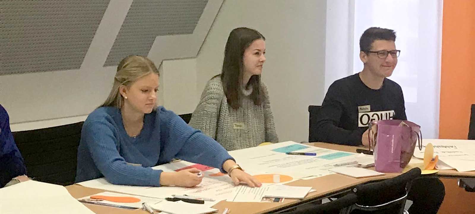 Schüler sitzen im Rechteck an Tischen