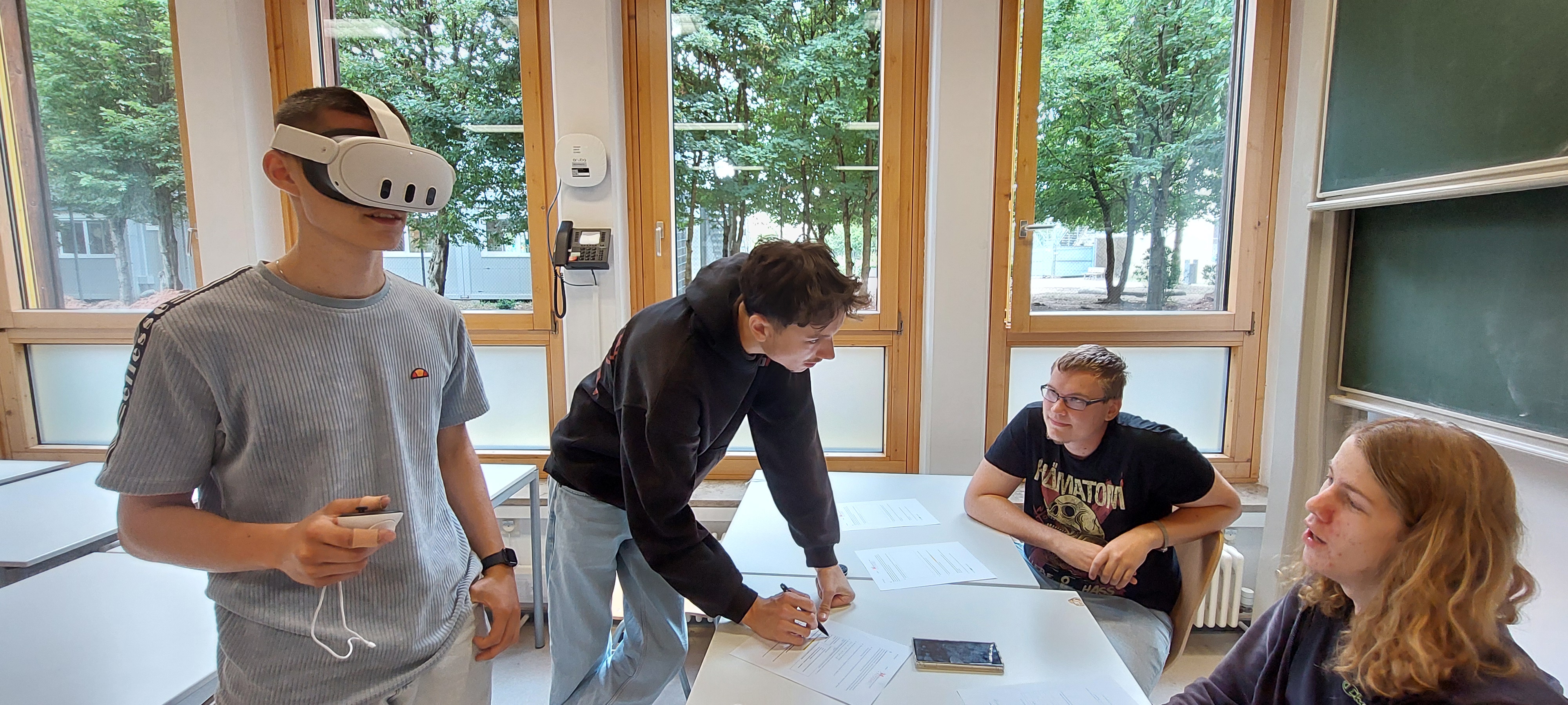 Ein Schüler mit VR-Brille im Klassenraum, drei weitere Schüler