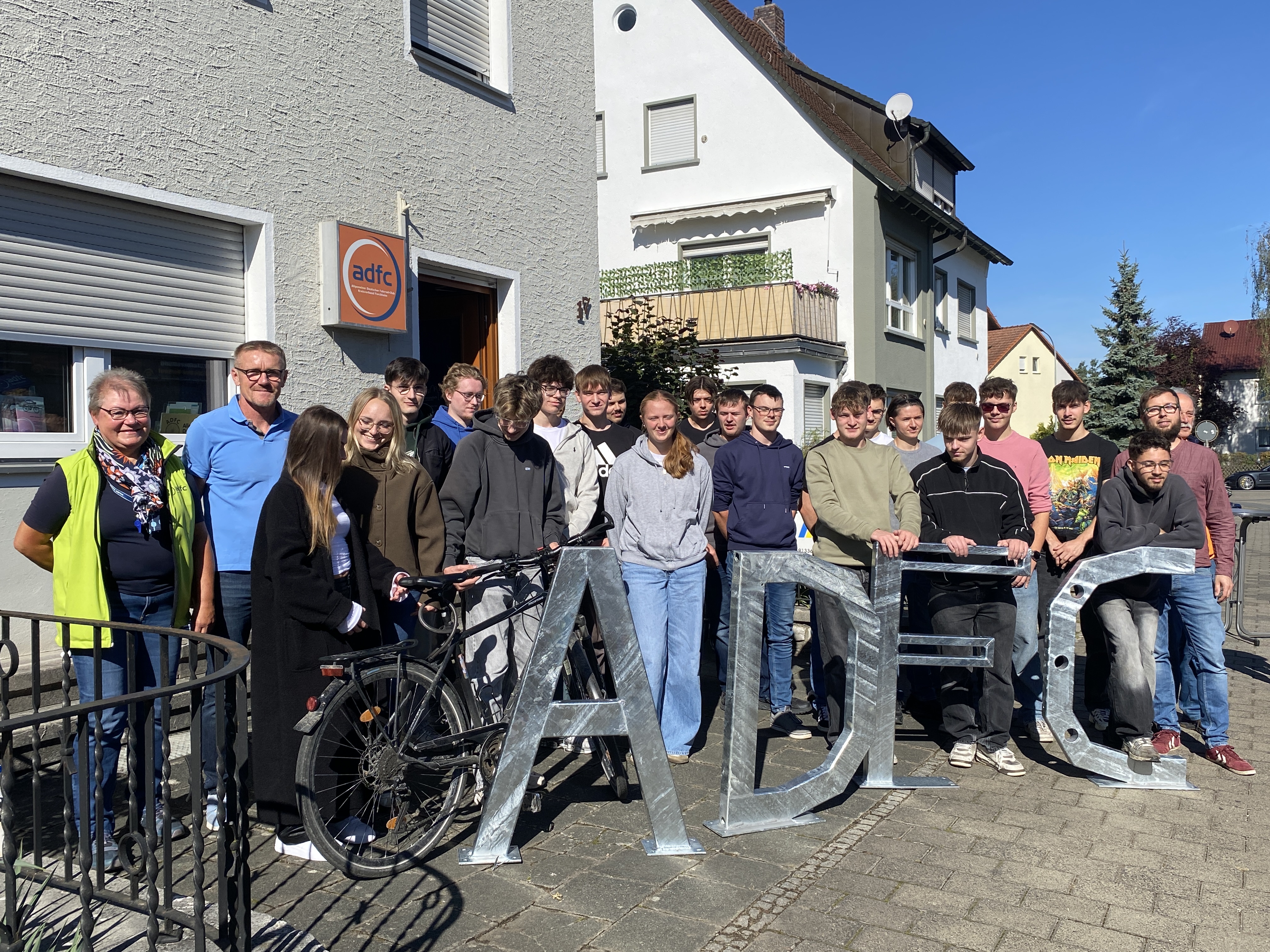 Vor dem Forchheimer Büro des „adfc“  stehen Schülerinnen und Schüler, die zwei Lehrkräfte und eine Vertreterin des „adfc“ und präsentieren die angefertigten Lettern „ADFC“
