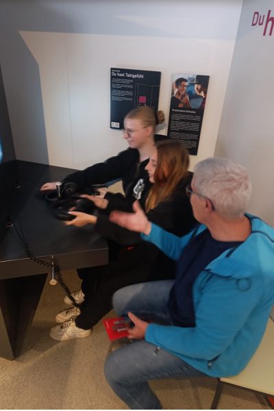 Schülerinnen und Lehrkraft sitzend vor PC