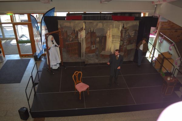 Blick auf die BÜhne, Stuhl im Vordergrund, drei Schauspielerinnen und Schauspieler