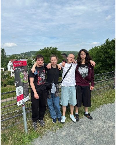 Gruppe Schülerinnen und Schüler vor  Themenschild; im Hintergrund Wiese und Bebauung
