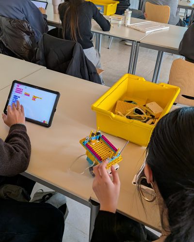 Lernende sitzend mit Legokisten und Legosteinen