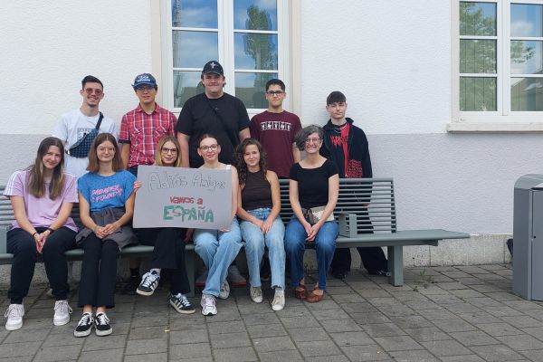Schülerinnen und Schüler mit Lehrerin sitzend vor Haus