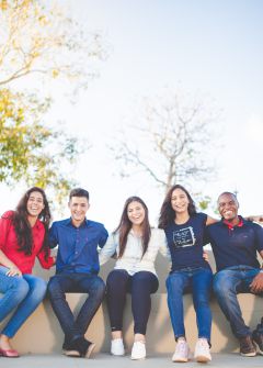 Gruppe junger Menschen sitzt auf Mauer und lacht