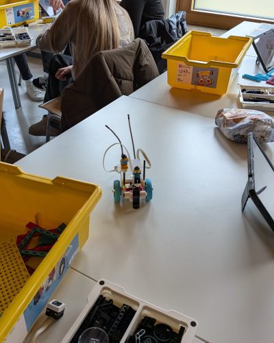 Schülerinnen sitzend, Legokisten und Legoroboter