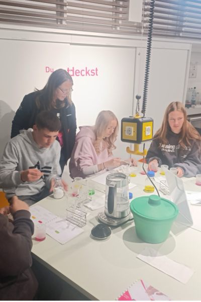 Schülergruppe sitzend um Tisch, mit verschiedenen Materialien darauf