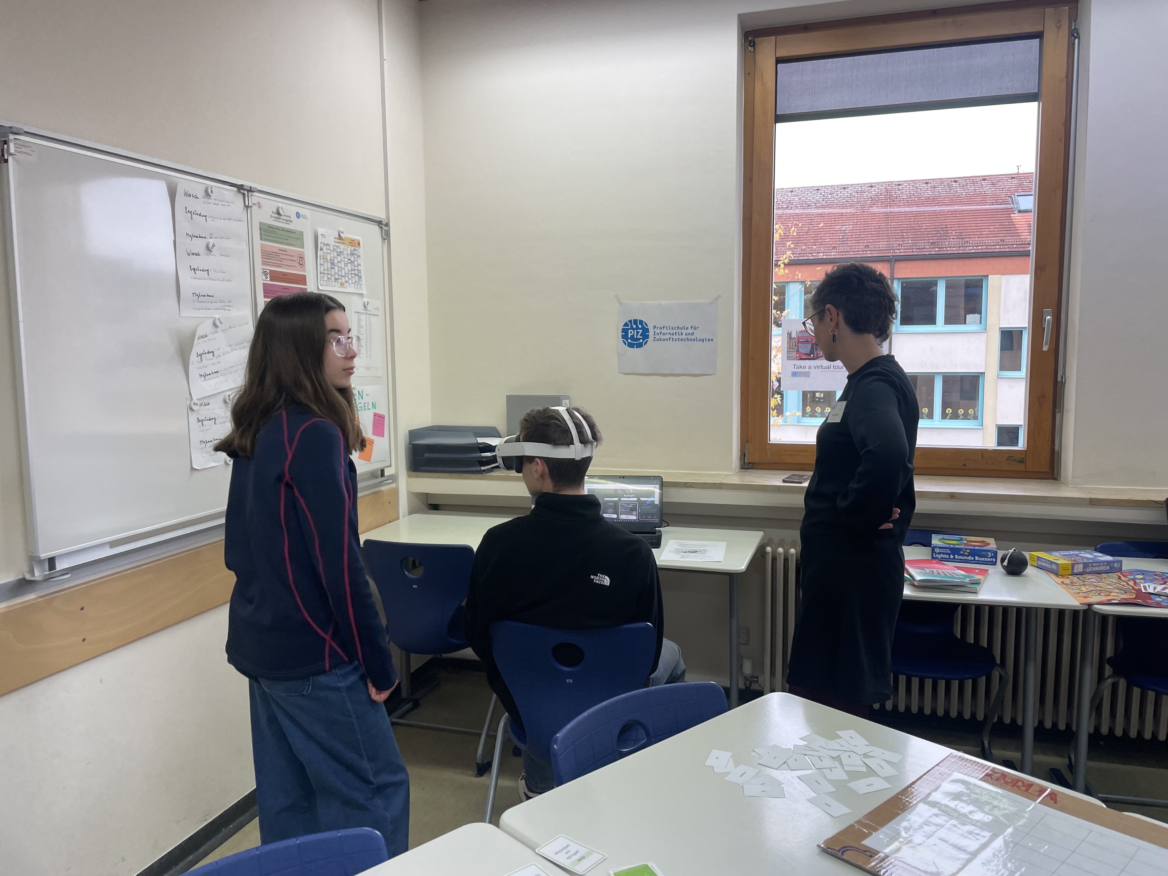 Person mit VR-Brille sitzend, zwei Personen stehend