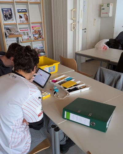 Schüler sitzend vor Tablet und Legosteinen